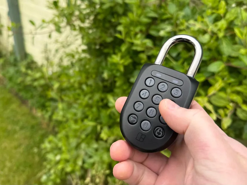 Person holding an Igloo smart padlock against a natural green foliage background